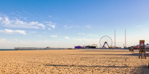 Empty beach with sand in full view and blue sky with amusement park in the distance.