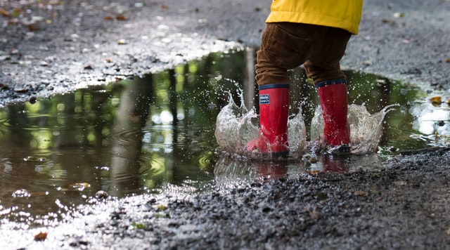 kid in red rainboots jumping in a puddle