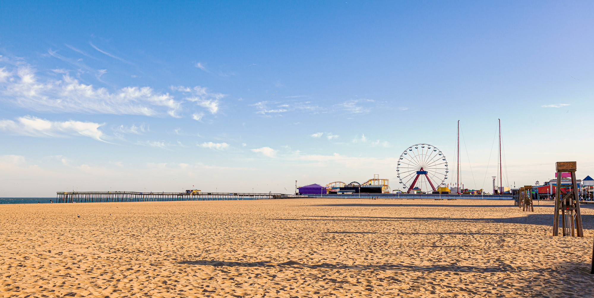 Empty beach with sand in full view and blue sky with amusement park in the distance.